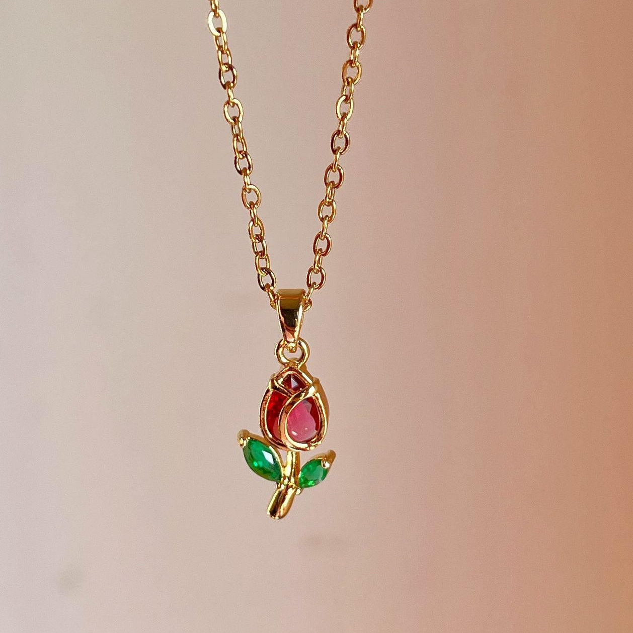 Gold necklace with a pendant featuring a red gem and green leaves on a blurred background