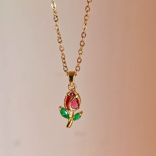 Gold necklace with a pendant featuring a red gem and green leaves on a blurred background