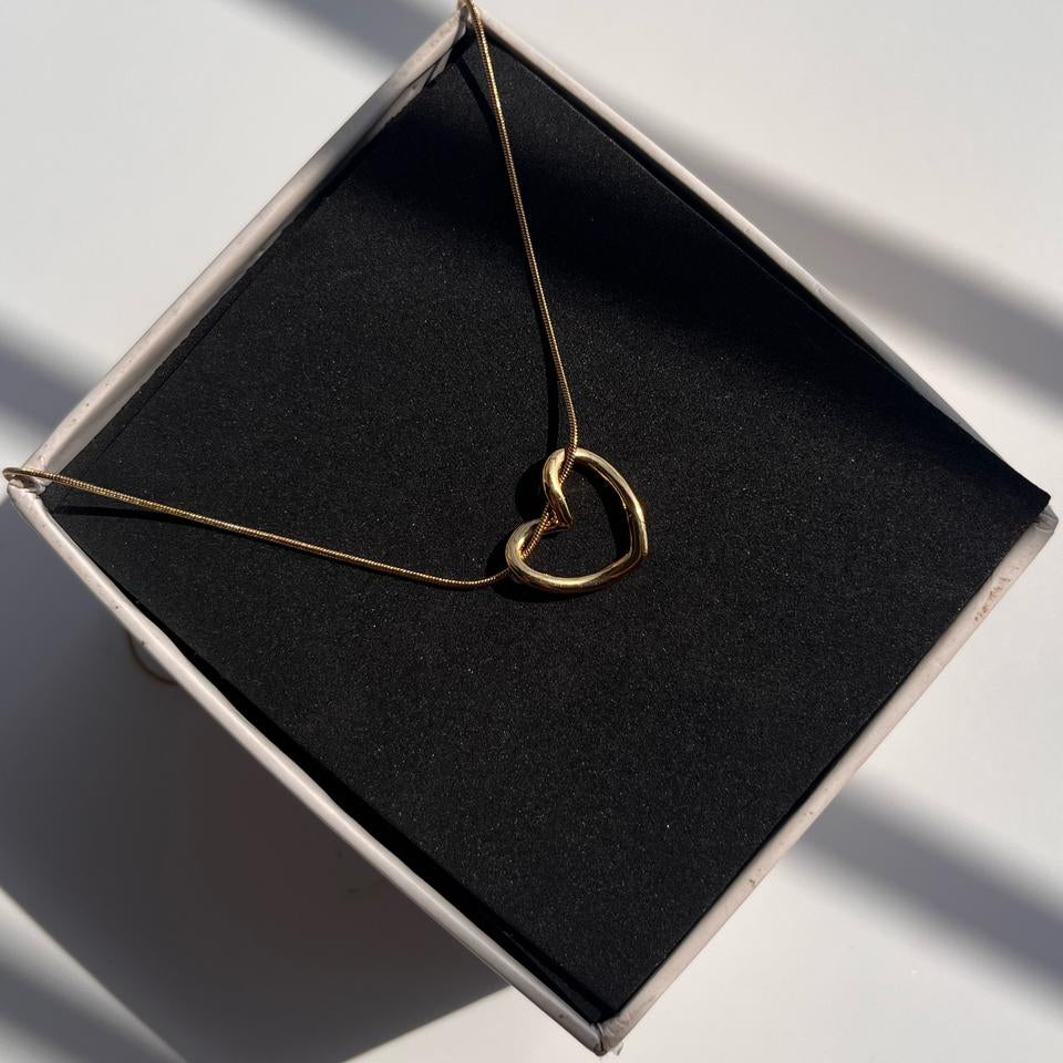 Gold heart-shaped necklace on a black box with soft shadows