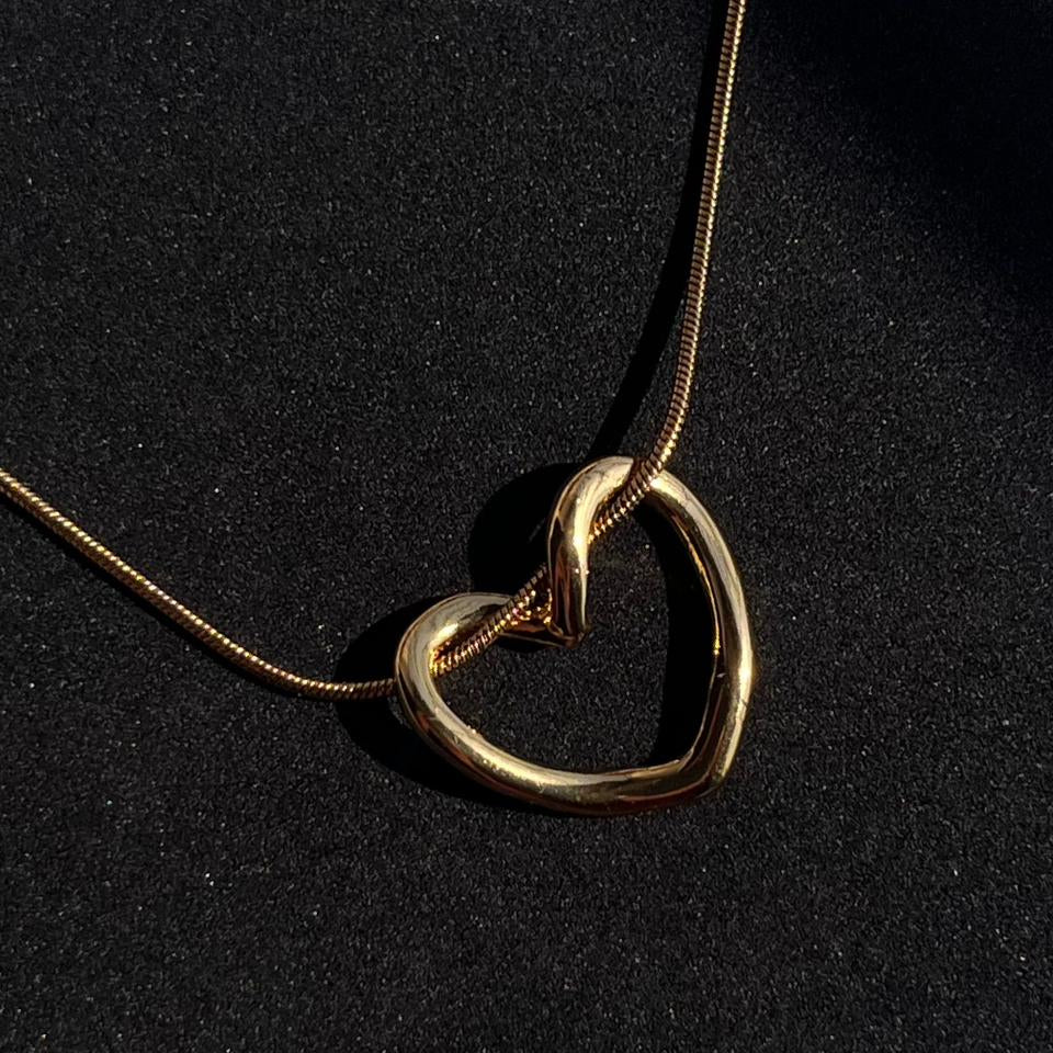 Gold necklace with a heart-shaped pendant on a black background