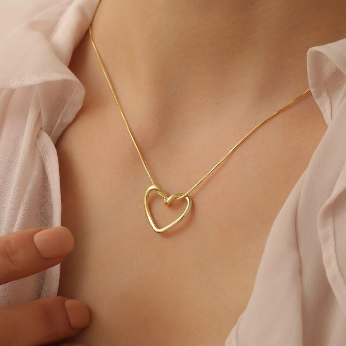 Gold heart-shaped necklace on a person wearing a light pink blouse.
