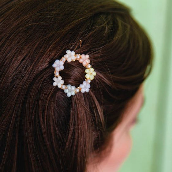 Close-up of a hair accessory with beads in a circular design on brown hair against a green background