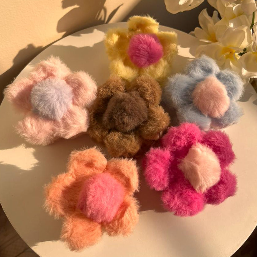 Colorful fluffy flower-shaped hair clips on a round surface with flowers in the background