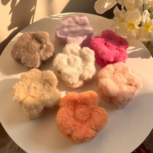 Colorful fuzzy hair clips on a white plate with flowers in the background