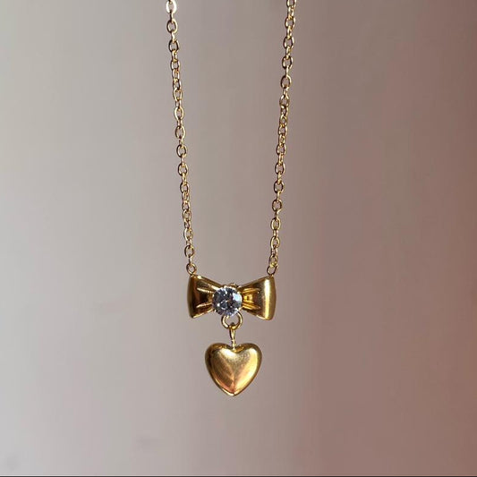 Gold necklace with a bow and heart pendant on a plain background