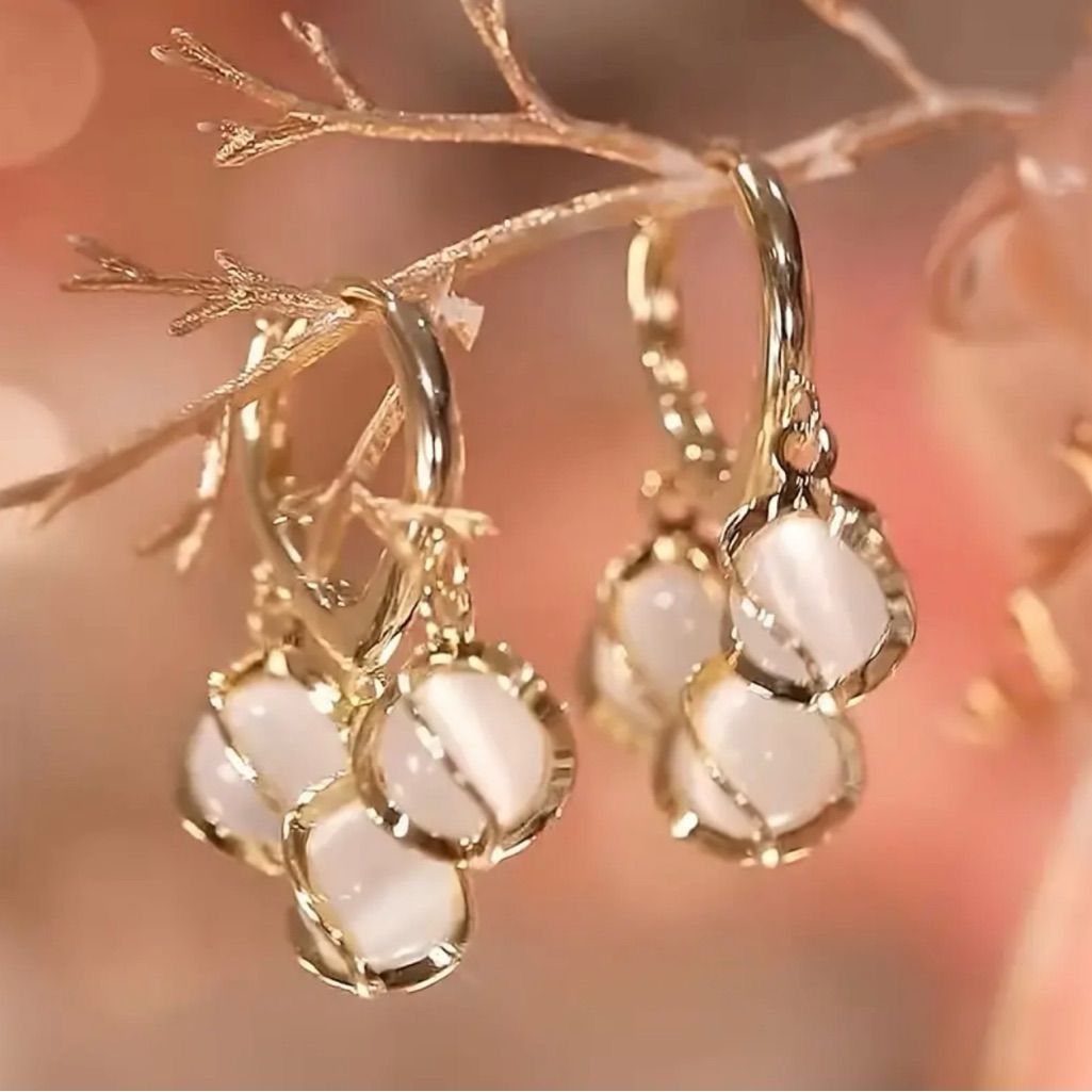 Gold earrings with white stones on a blurred background