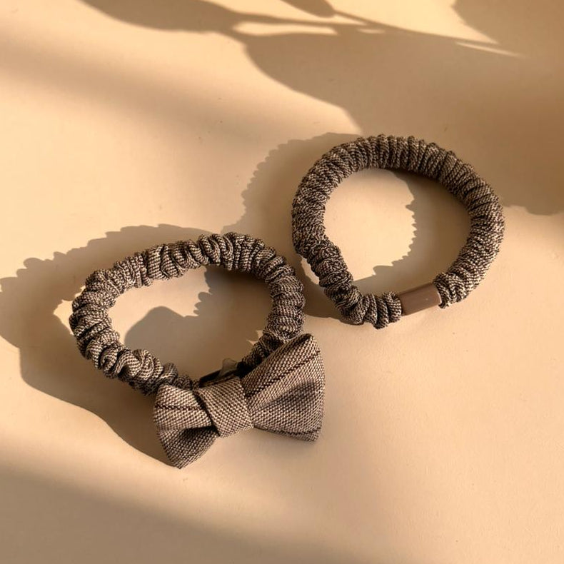 Two gray hair scrunchies with a bow on a beige surface