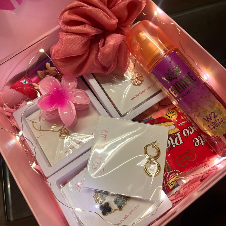 Pink gift box with hair scrunchie, earrings, and other items on a dark surface