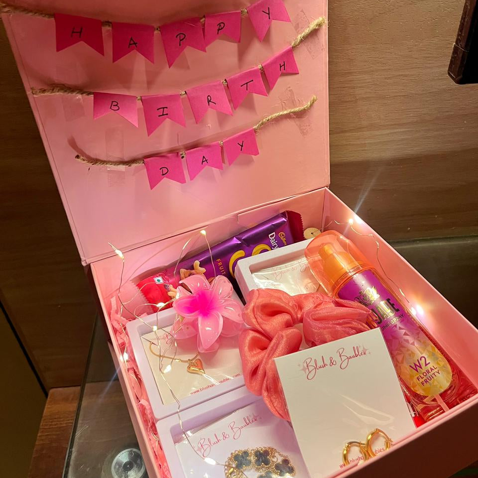 Pink birthday gift box with various items including a hair tie, card, and small bottles.
