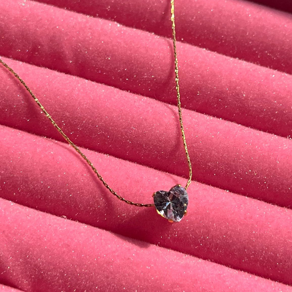 Heart-shaped purple gemstone necklace on a pink textured surface