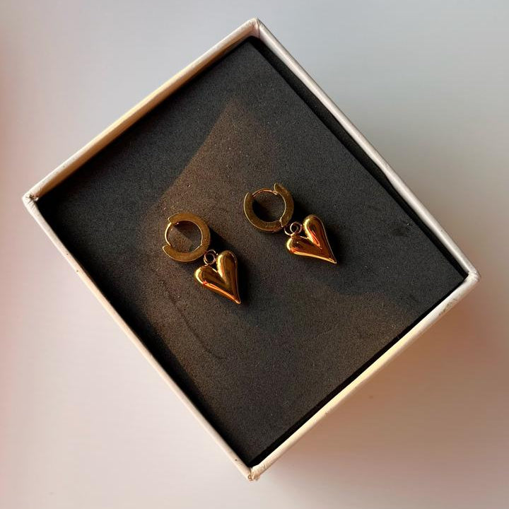 Heart-shaped gold earrings in a box on a light background
