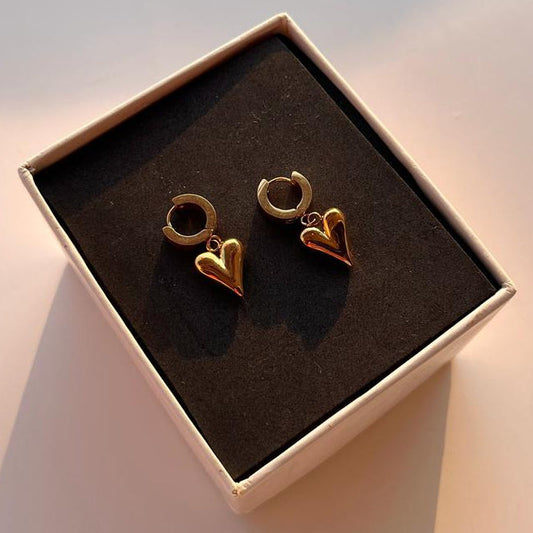 Gold heart-shaped earrings in a box on a light background