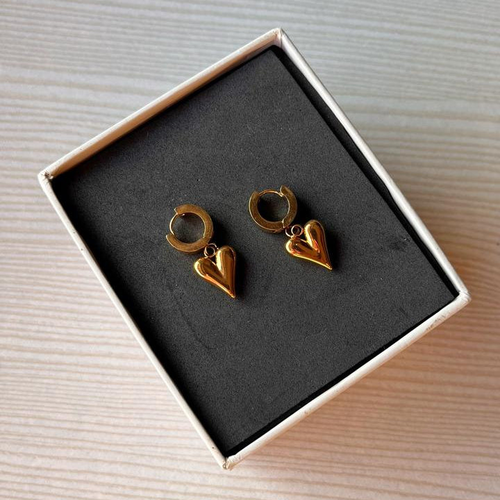 Heart-shaped gold earrings in a box on a textured surface