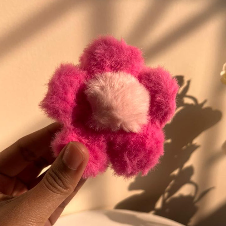 Hand holding a pink fuzzy flower against a neutral background