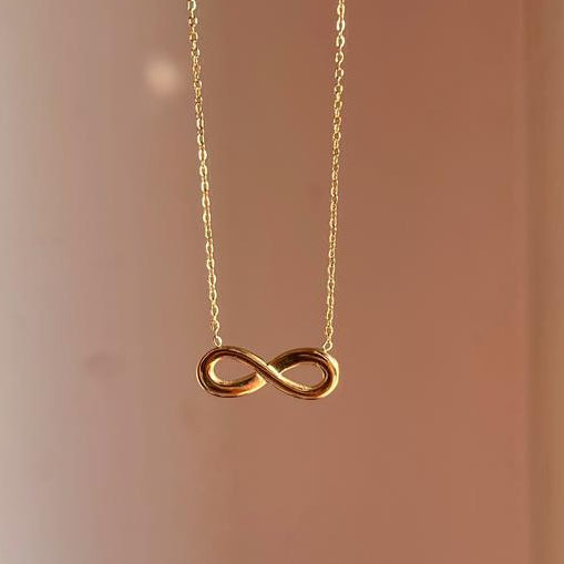 Gold infinity necklace on a plain background
