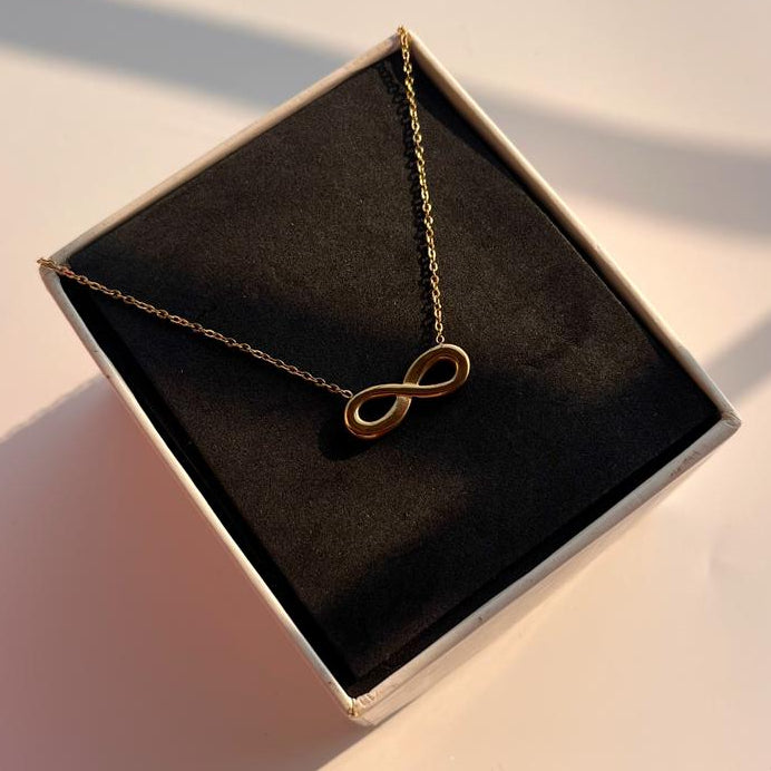 Gold infinity necklace in a black box on a light surface