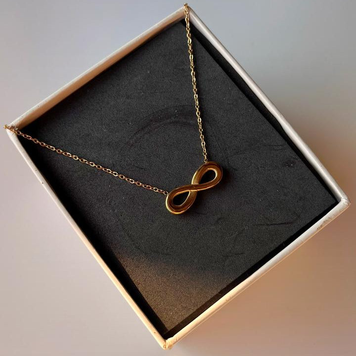 Gold infinity necklace in a box on a soft focus background