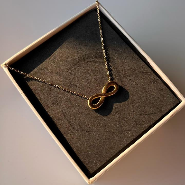 Gold infinity necklace in a box on a neutral background