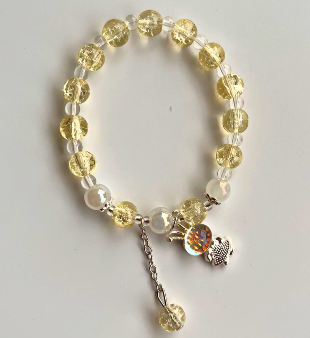 Bracelet with yellow beads and a silver charm on a light gray background