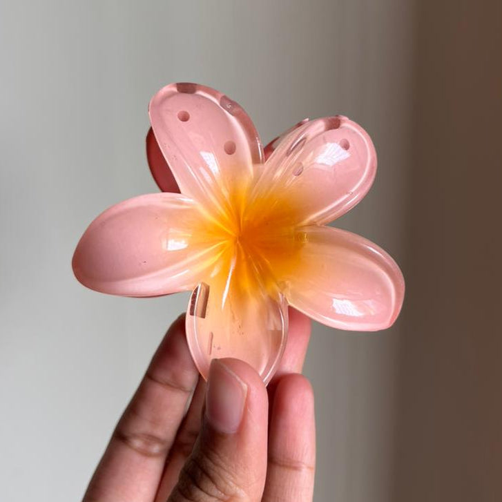 Hand holding a orange flower-shaped hair clip against a plain background