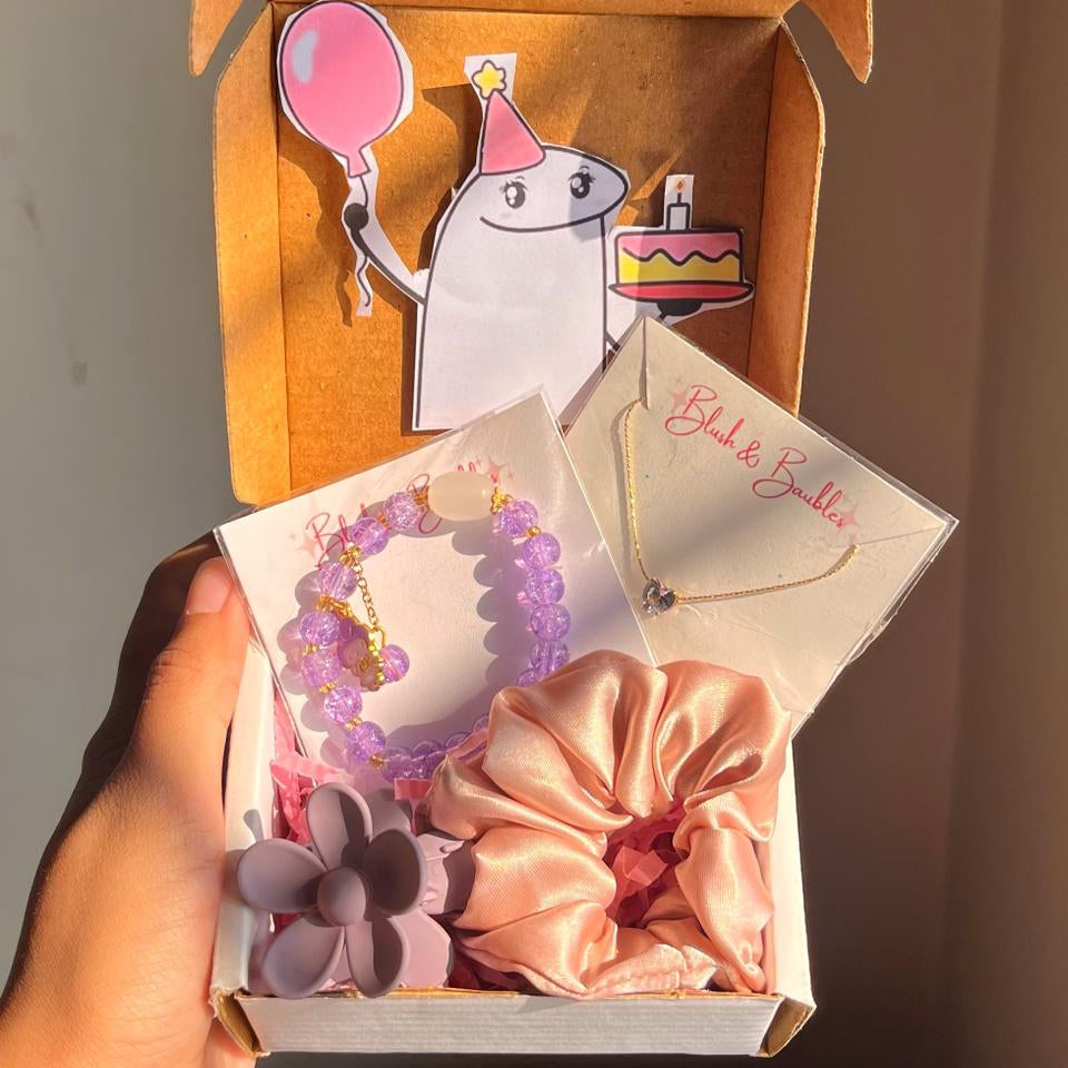 Gift box with decorative items including jewellery and hair accessories, held against a neutral background.