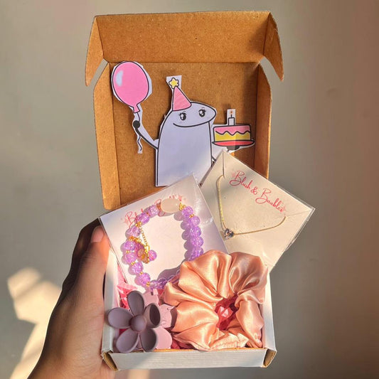 Gift box with decorative items including a bow, necklace, bracelet, and a card, held by a hand.