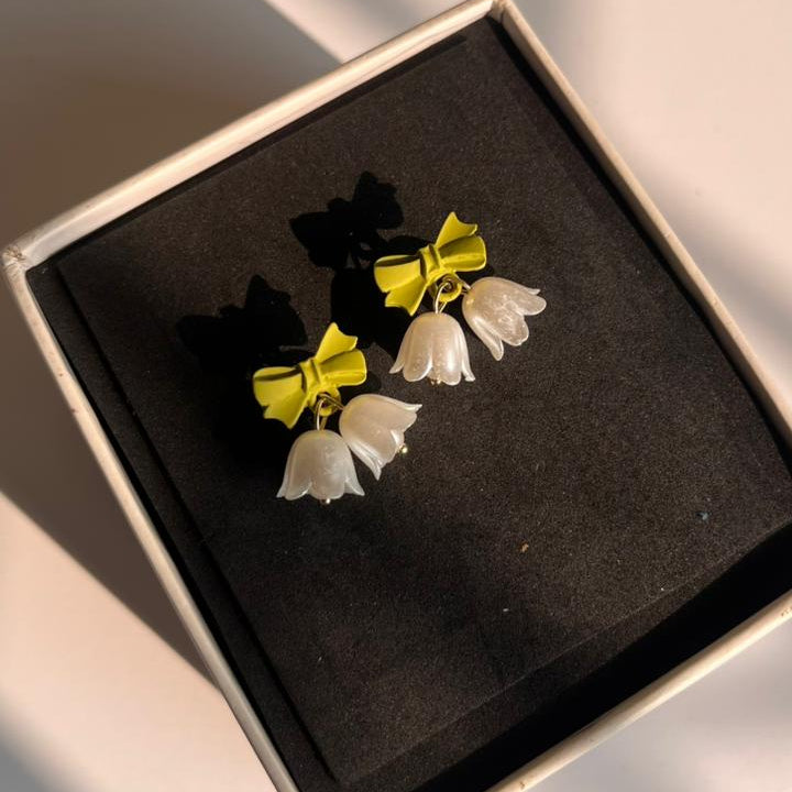 Yellow and white bow-shaped earrings in a box on a light surface