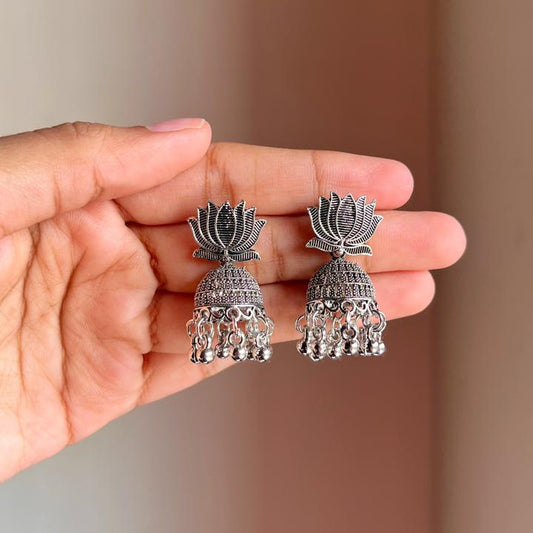 Silver lotus-shaped earrings held between fingers against a blurred background