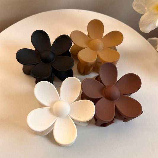 Set of four flower-shaped hair clips in black, brown, beige, and white on a light surface.