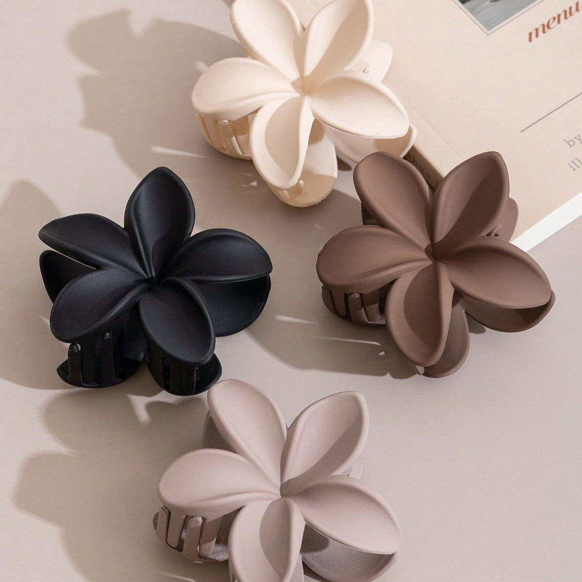 Four floral-shaped hair clips in black, beige, brown, and gray on a light surface.