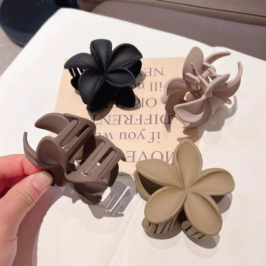 Set of four floral-shaped hair clips in black, brown, and beige on a magazine page.