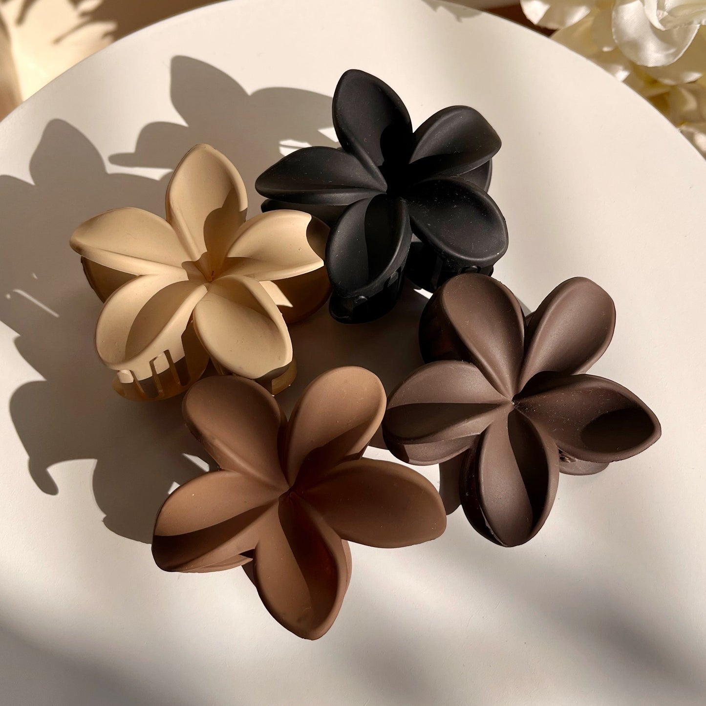 Set of three flower-shaped hair clips in black, beige, and brown on a white plate.