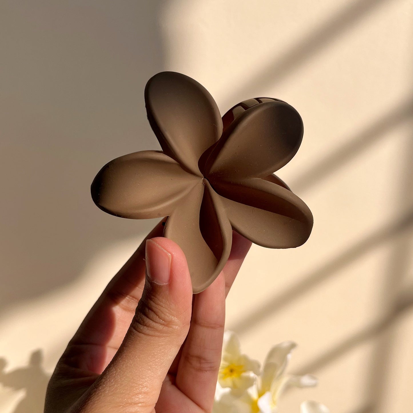 Hand holding a brown floral clip against a neutral background
