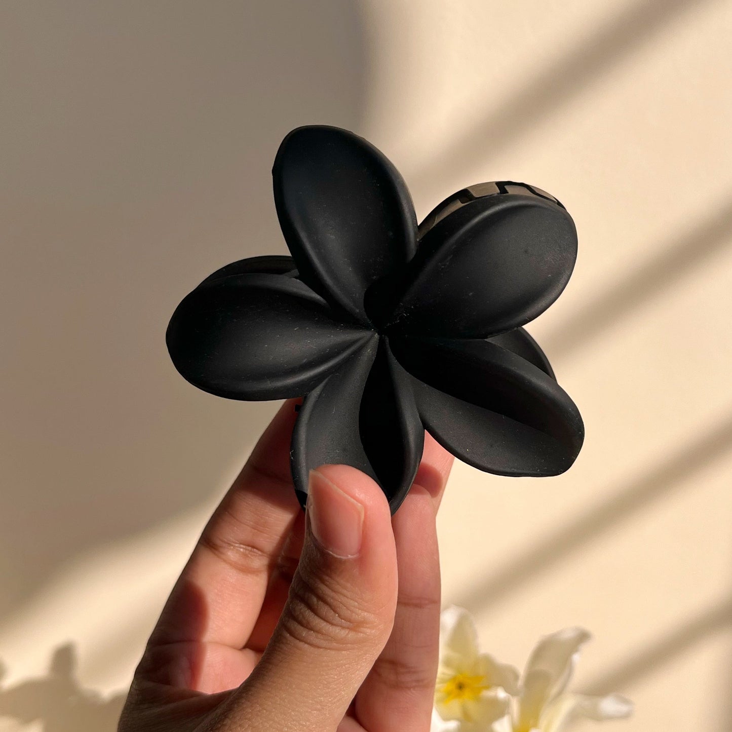 Black flower-shaped hair clip held by a hand with a neutral background