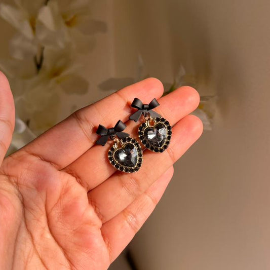 Hand holding a pair of black and gold earrings with a neutral background