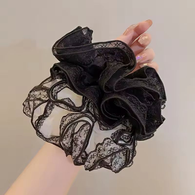 Black lace scrunchie held by a hand against a neutral background
