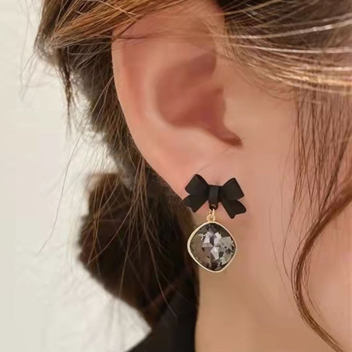 Close-up of an ear wearing a black bow earring with a gemstone pendant.