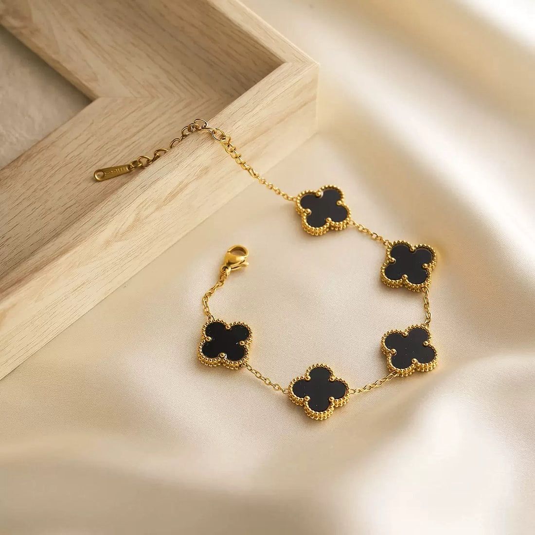 Gold bracelet with black clover-shaped charms on a wooden surface