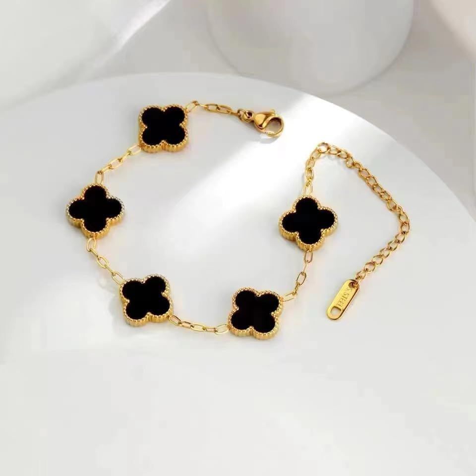 Gold bracelet with black clover-shaped charms on a white background