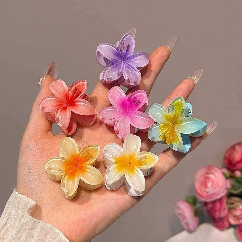 Hand holding colorful flower-shaped hair clips against a neutral background