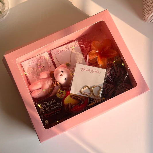 Pink gift box with a variety of items including a jewellery products, keychain, hair accessories and a cookie box.