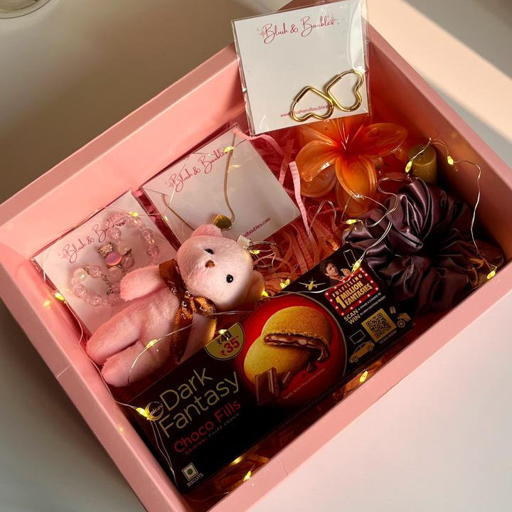 Pink gift box with chocolate, a small pink keychain, and a card on a light surface.