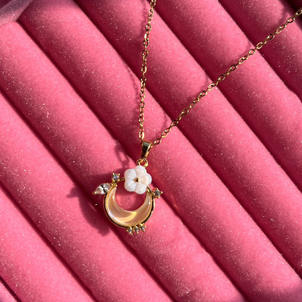 Gold necklace with a crescent moon and flower pendant on a pink velvet surface