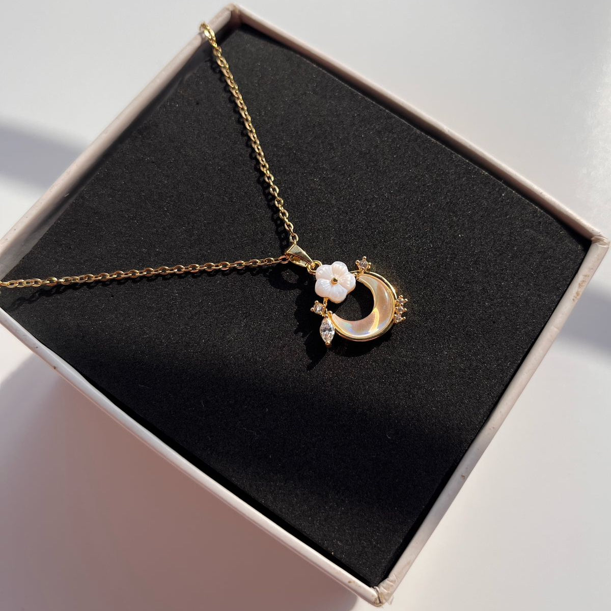 Gold necklace with a crescent moon and star pendant on a black jewelry box.