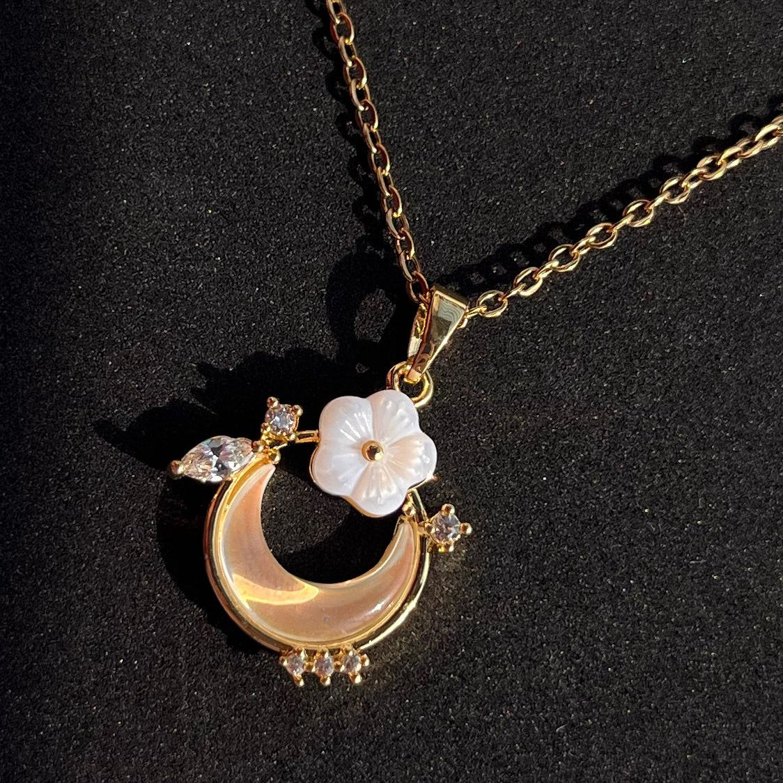 Gold necklace with a crescent moon and floral pendant on a black background