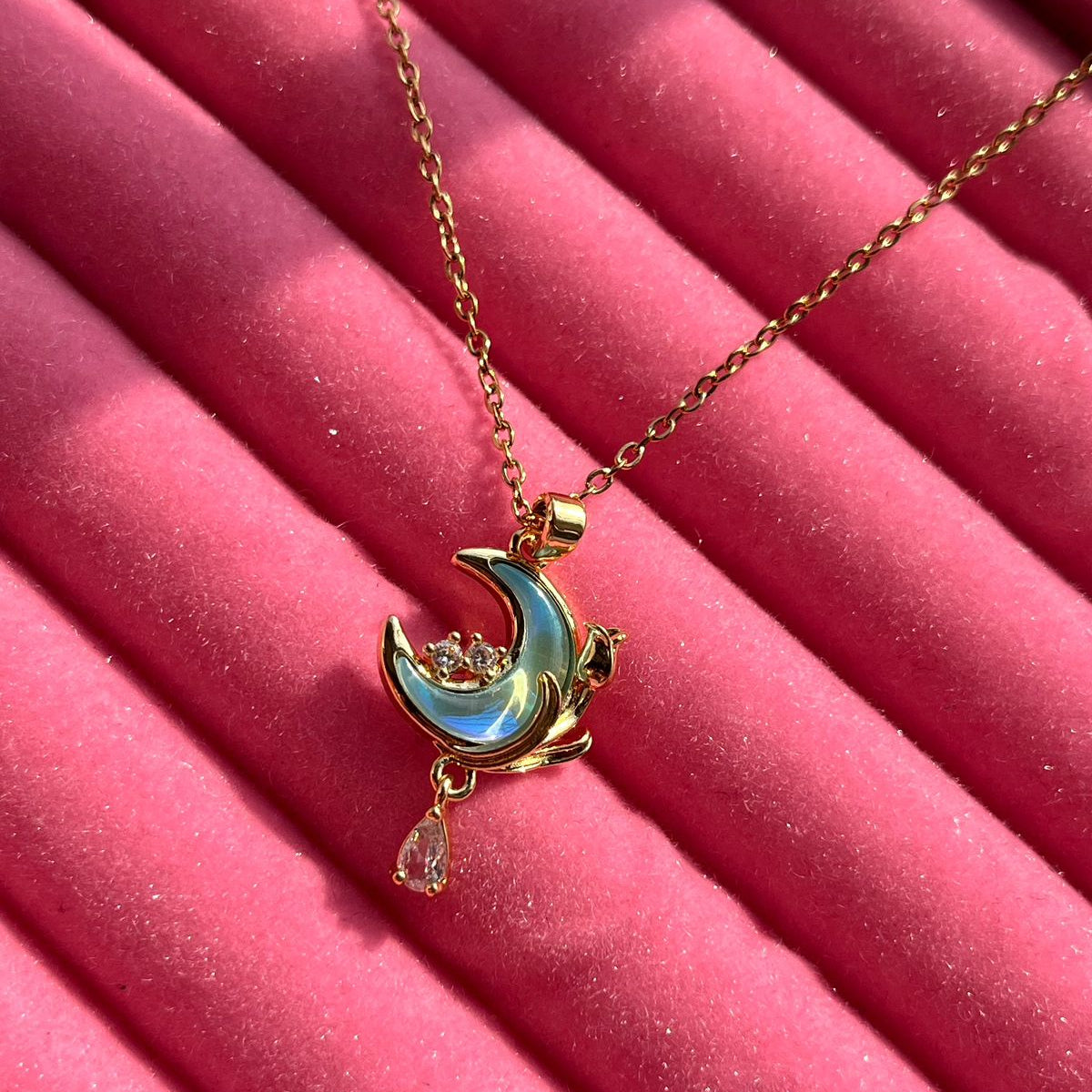 Gold necklace with a moon and star pendant on a pink surface