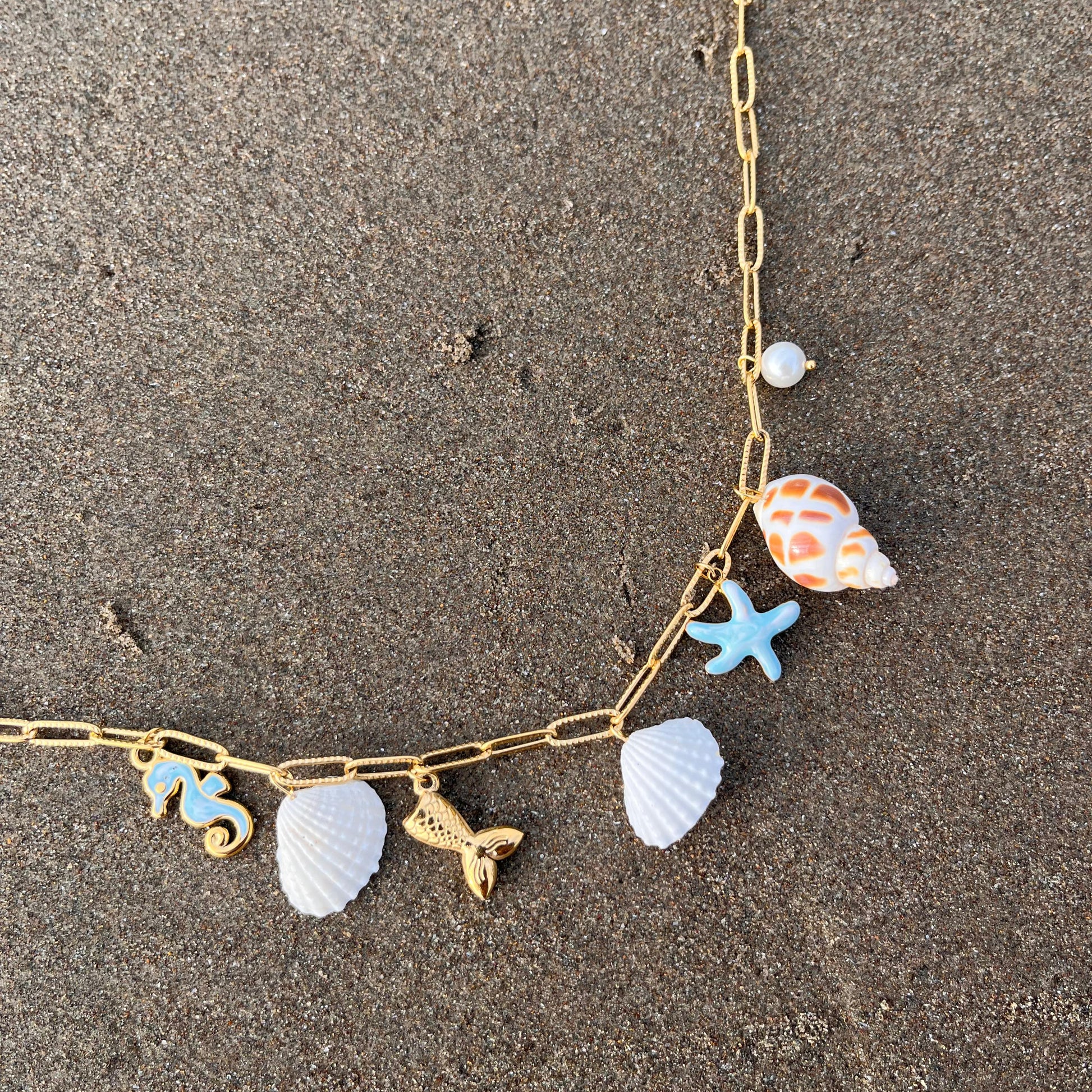 Necklace with shell and starfish charms on a sandy surface