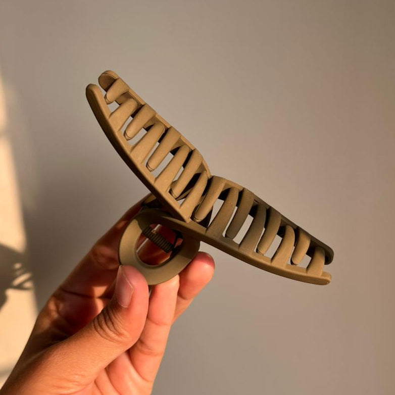 Hand holding a brown hair clip against a plain background