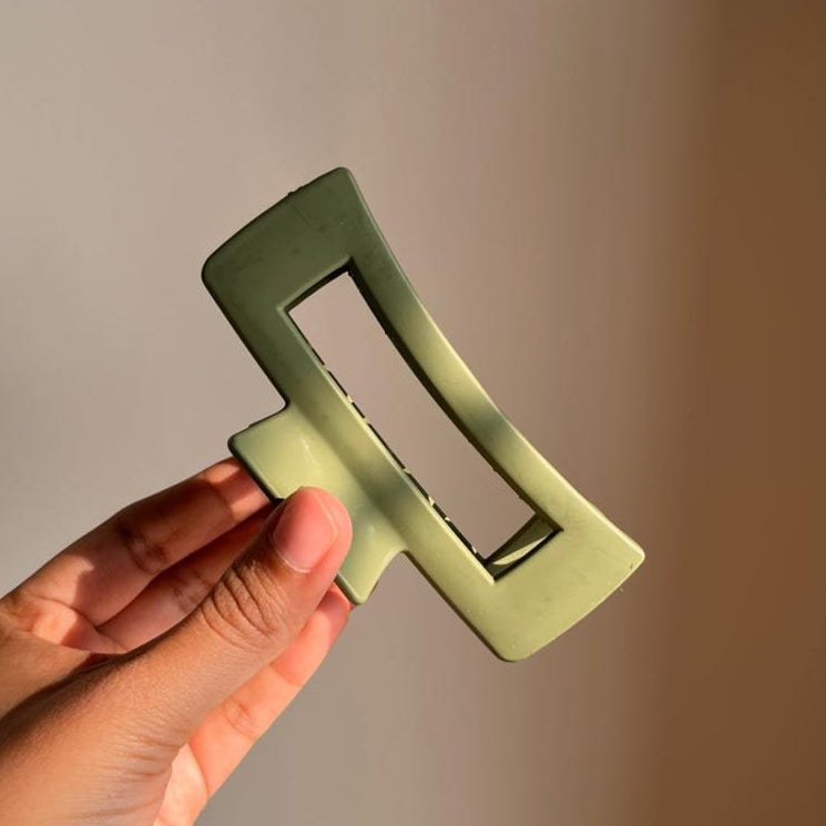 Hand holding a green hair clip against a plain background