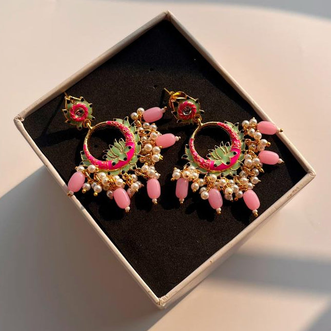 Decorative earrings with pink and green details in a box on a light surface